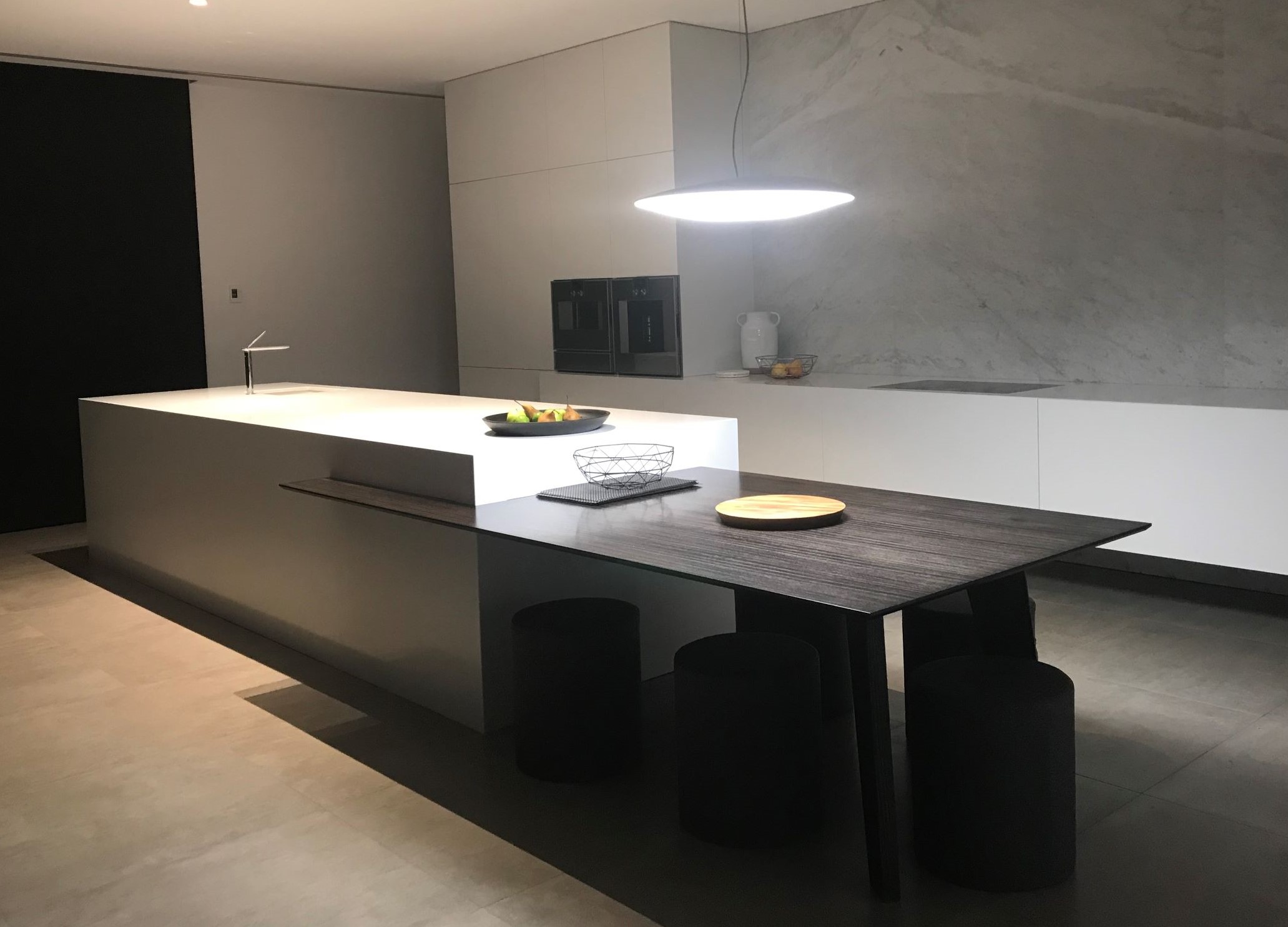 Stone bench top with wooden seating area and marble splashback. Large pendant light over benchspace