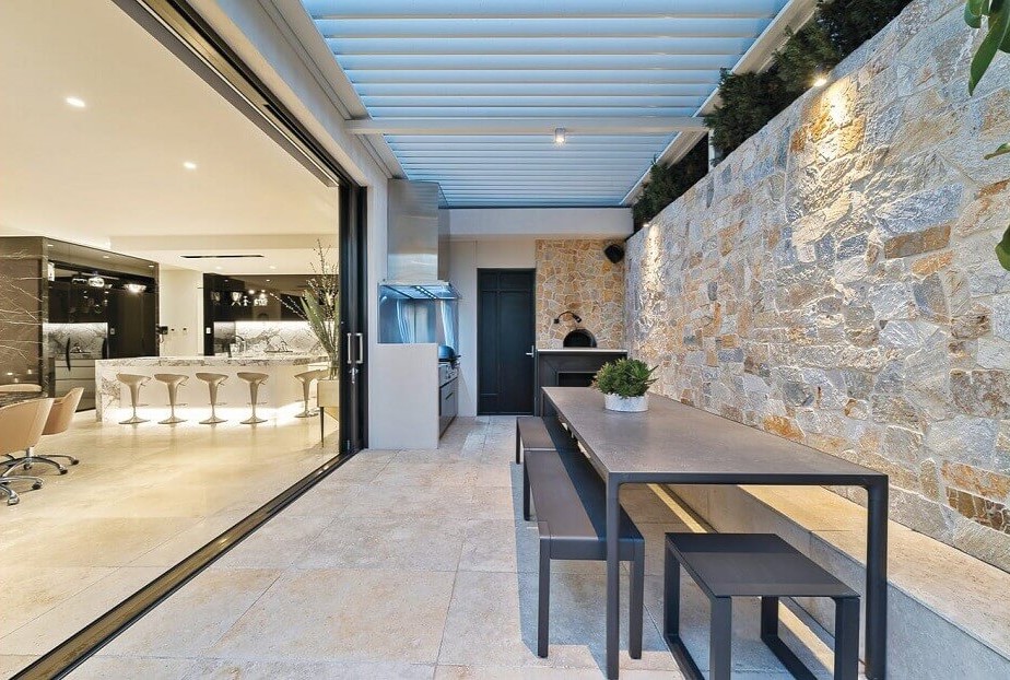 Luxury outdoors entertaining area with sandstone wall and open doors into the kitchen space 